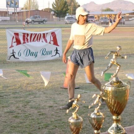 Runner at the Arizona 6 Day Run finish with trophies in the foreground.
