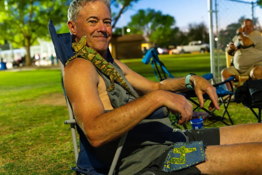 Dave Nevins sitting in a chair with a chameleon on his shoulder at the Arizona 6 Day Race.